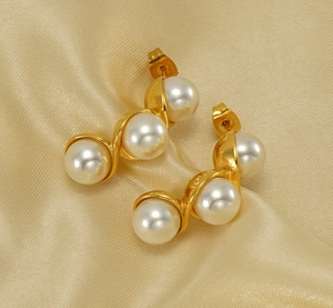 Macro shot of gold S-shaped wave earrings with three white pearls on silk background