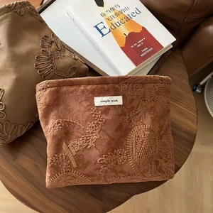 Detail of camel brown faux suede cosmetic bag with floral embroidery and textile label