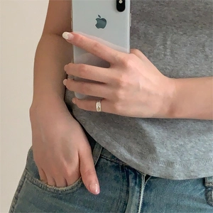 Close-up of a silver ring with cutout heart patterns worn by a model in a casual setting