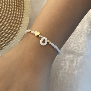 Detail of beaded bracelet with gold heart and shell disc featuring the letter O
