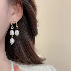 Close-up of elegant gold drop earrings with three pearls worn by a model in warm light