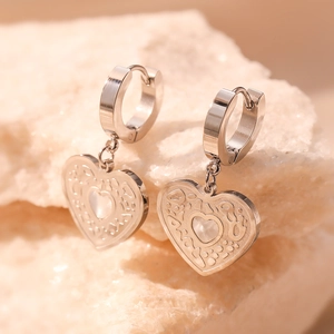 Silver heart earrings with mother of pearl inlay displayed on a textured stone base