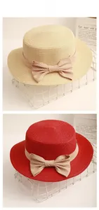 Detail of flat top straw boater hats in beige and red with striped ribbon bow decoration