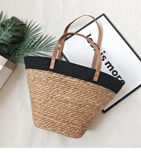 Close-up of woven straw tote bag featuring black fabric trim and brown PU leather straps