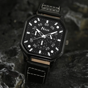 Close-up of a square black dial watch with leather strap on dark rock texture