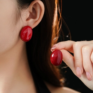 Detail of red oval enamel stud earring with glossy finish shown on model's ear