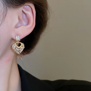 Close-up of heart-shaped gold earrings with sparkling pavé cubic zirconia on ear lobe