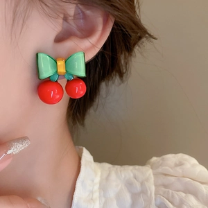 Gros plan d'un mannequin portant des boucles d'oreilles cerises rouges avec nœud papillon