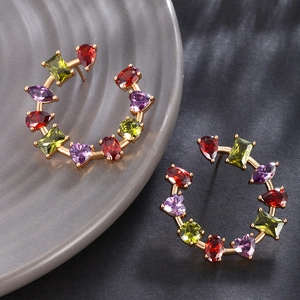 Macro shot of C-shaped gold earrings with colorful heart and teardrop zircon crystals