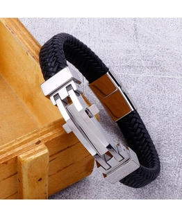 Detail of black woven leather men's bracelet with polished metal clasp on a wooden box