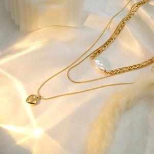 Detail of 18k gold triple-layered necklace with heart pendant and pearl on white silk