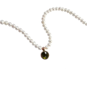 Detail of white pearl necklace with dark gemstone pendant and golden metal rim