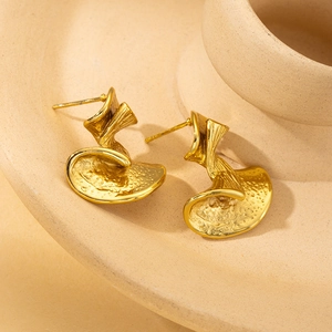 Vintage irregular golden leaf stud earrings with hammered texture on beige ceramic base