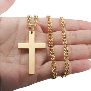 Minimalist gold cross necklace with Cuban chain held against a clean white background