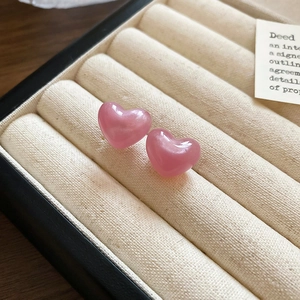 Macro shot of pink heart stud earrings with cat eye resin finish in a beige jewelry box