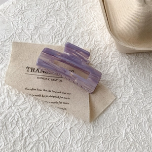 Close-up of a rectangular purple marble acetate hair claw clip on a beige fabric card