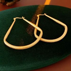 Détail macro de boucles d'oreilles dorées en éventail avec texture mate sur velours