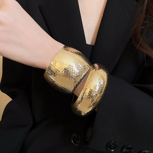 Detail view of gold textured hammered cuff bracelet on model wearing black suit