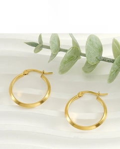 Detailaufnahme goldener 18K Edelstahl-Creolen mit gebürstetem Finish auf Wellenhintergrund