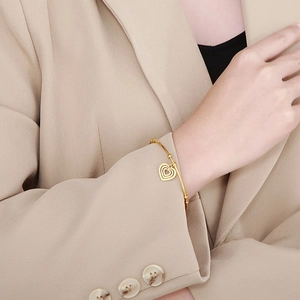Detail of gold heart pendant bangle on model with beaded band and metallic finish