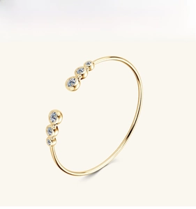 Dettaglio di un bracciale rigido dorato minimalista con sei pietre preziose scintillanti
