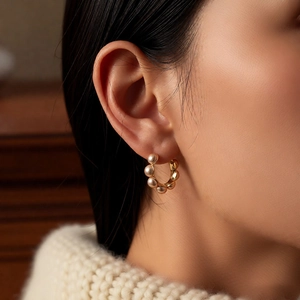 Gros plan de boucles d'oreilles créoles dorées 18K avec perles et pull beige