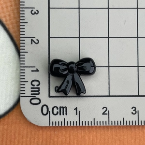 Close-up of a 1.5cm black resin bow accessory on a grid ruler for size measurement