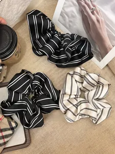 Detailed view of striped satin scrunchies with smooth pleated texture in black and white