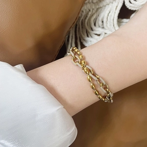 Bracelet double couche en maille dorée avec émail blanc et perles sur le poignet