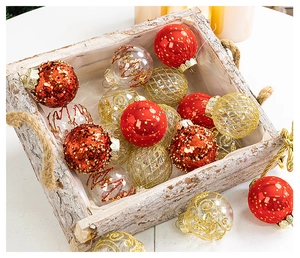 Assorted red and gold Christmas ornaments displayed in a rustic bark box with warm candles