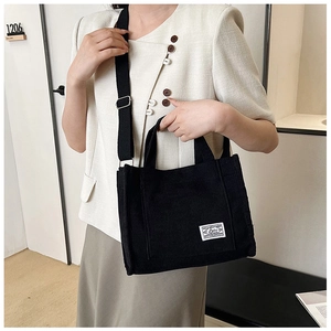 Model wearing a large capacity black corduroy square bag with white patch label
