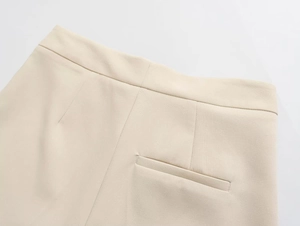 Detailed view of beige tailored trousers featuring a neat waist cut and welt pockets