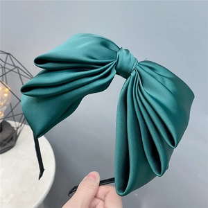 Detailed close-up of dark green satin triple-layered bow headband with silk texture