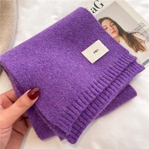 Detail view of purple knitted scarf texture and small beige woven label with emo text