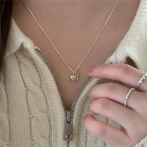 Close-up of 925 silver heart and key pendant necklace with minimalist rings on a knit sweater