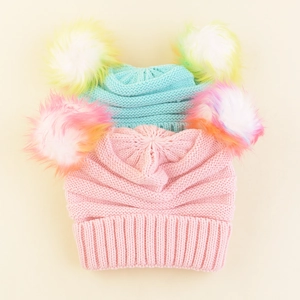 Close-up of pink and blue knit hats with large rainbow faux fur pompoms on beige background