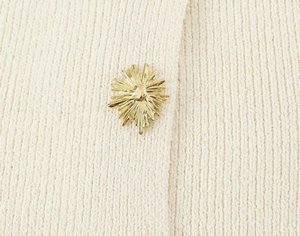 Détail macro d'un bouton doré soleil sur le tissu en maille beige d'un pull chic