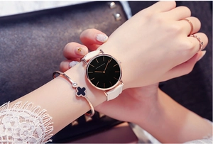 Elegant quartz watch with black dial, white leather strap and clover bracelet on wrist