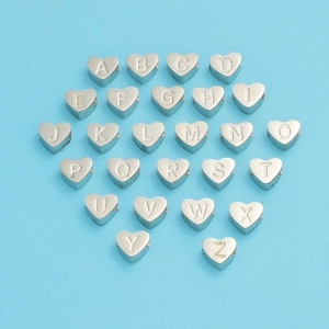 Vue macro de 26 perles de coeur argentées avec gravures alphabet A-Z sur fond bleu clair