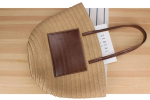 Detail view of straw woven tote bag with brown leather patch on a wooden table