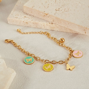 Detailed view of golden butterfly bracelet with colorful enamel charms on a stone display