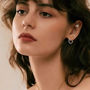 Close-up of polished silver hoop earrings and sparkling zircon studs on a female model