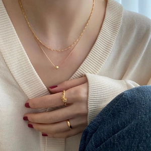 Detail of layered gold heart necklace and knot ring worn with a casual knit cardigan