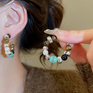 Detail view of retro C-shaped earrings with tiger eye, pearls, and turquoise beads