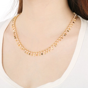 Detail of gold necklace with small teardrop metal charms and peach beads on neck