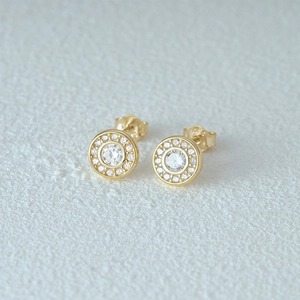 Close-up of golden halo stud earrings with zircon crystals on white texture