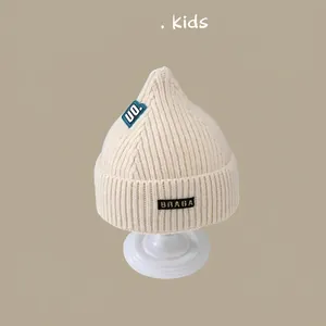 Detail of cream knitted baby hat with soft ribbed texture and decorative woven labels