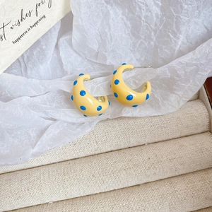Macro detail of dopamine-style C-shaped yellow earrings with dark blue polka dots