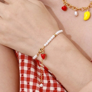 Detail of a pearl bracelet featuring a red strawberry charm on a female model wrist