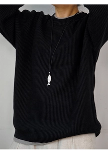 Detail of silver fish pendant necklace on black waffle knit sweater with crew neck
